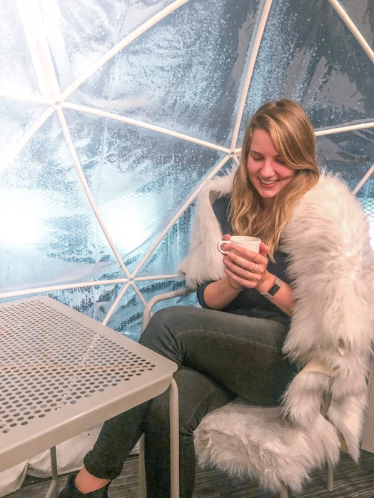A woman smiles while holding a mug and sitting on a fuzzy chair at an igloo bar.