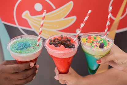 Three women's hands hold out colorful slushies in plastic cones, which are served at the 2020 Epcot ...