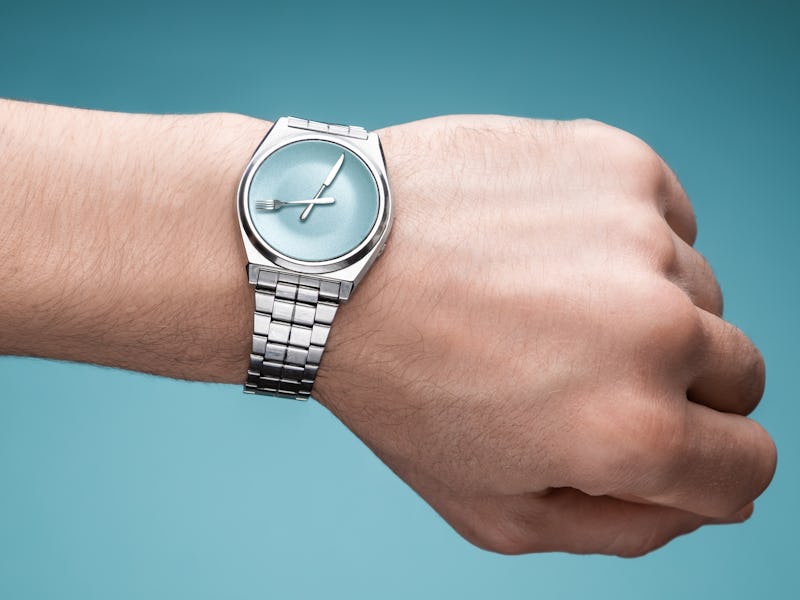An illustration of a man's hand with a watch that has a spoon and a fork as pointers representing al...