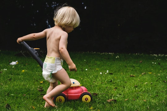 Child wearing diaper pushes a toy lawnmower