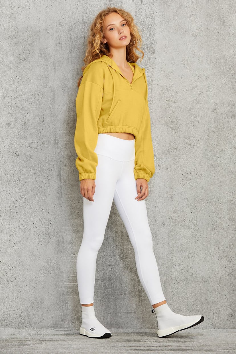 A girl posing in a yellow sports hoodie and in white leggings