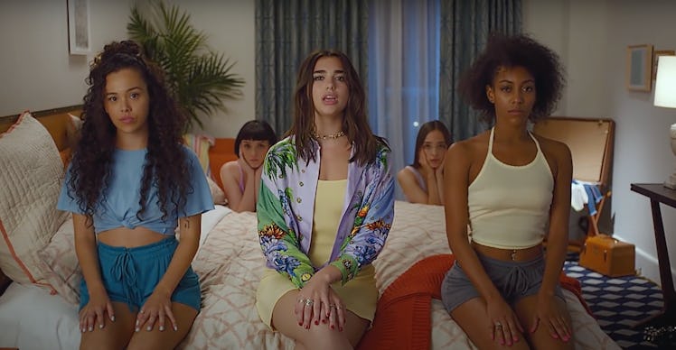 Dua Lipa's music video for "New Rules" features women sitting in colorful outfits on a hotel bed.