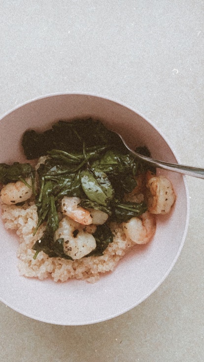 A bowl of shrimp, spinach, and quinoa sits on a kitchen counter.