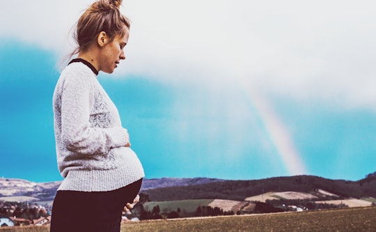 A pregnant woman stands by a rainbow