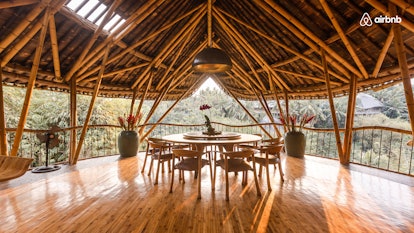 A bamboo house in Bali, Indonesia has a round table with chair all around, overlooking nature. 
