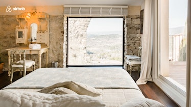 A home in France has rock walls and a white linen bed overlooking nature. 