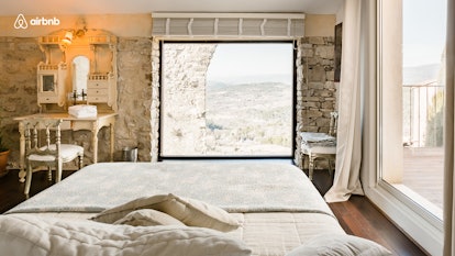 A home in France has rock walls and a white linen bed overlooking nature. 