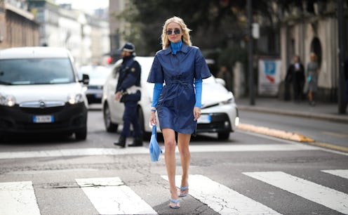 A woman walking down the street in a dark blue suit, with a turtleneck underneath and thong sandals