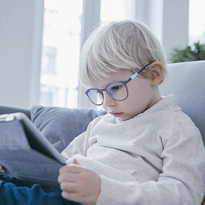 Little boy looking down at a tablet while wearing blue light blocking glasses