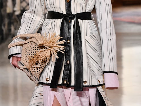 A closeup of a model holding a woven bag while walking the runway