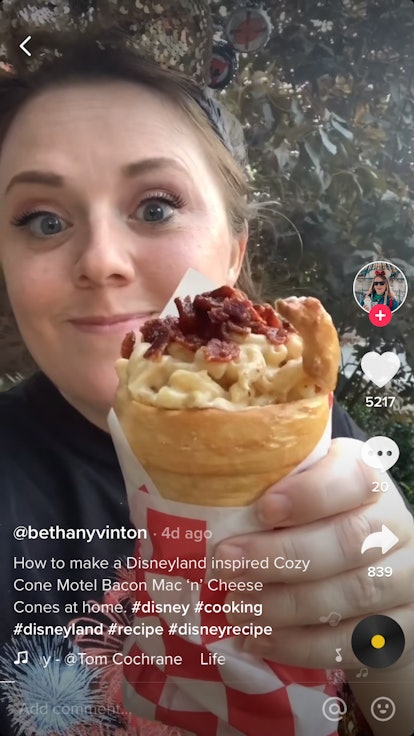 A woman wearing Mickey ears holds a bacon mac 'n' cheese cone. 