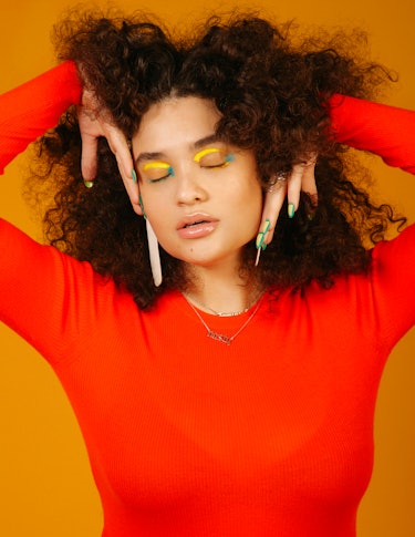 Diana Veras wearing an orange Courrages knit light sweater with Avery Gregory earrings