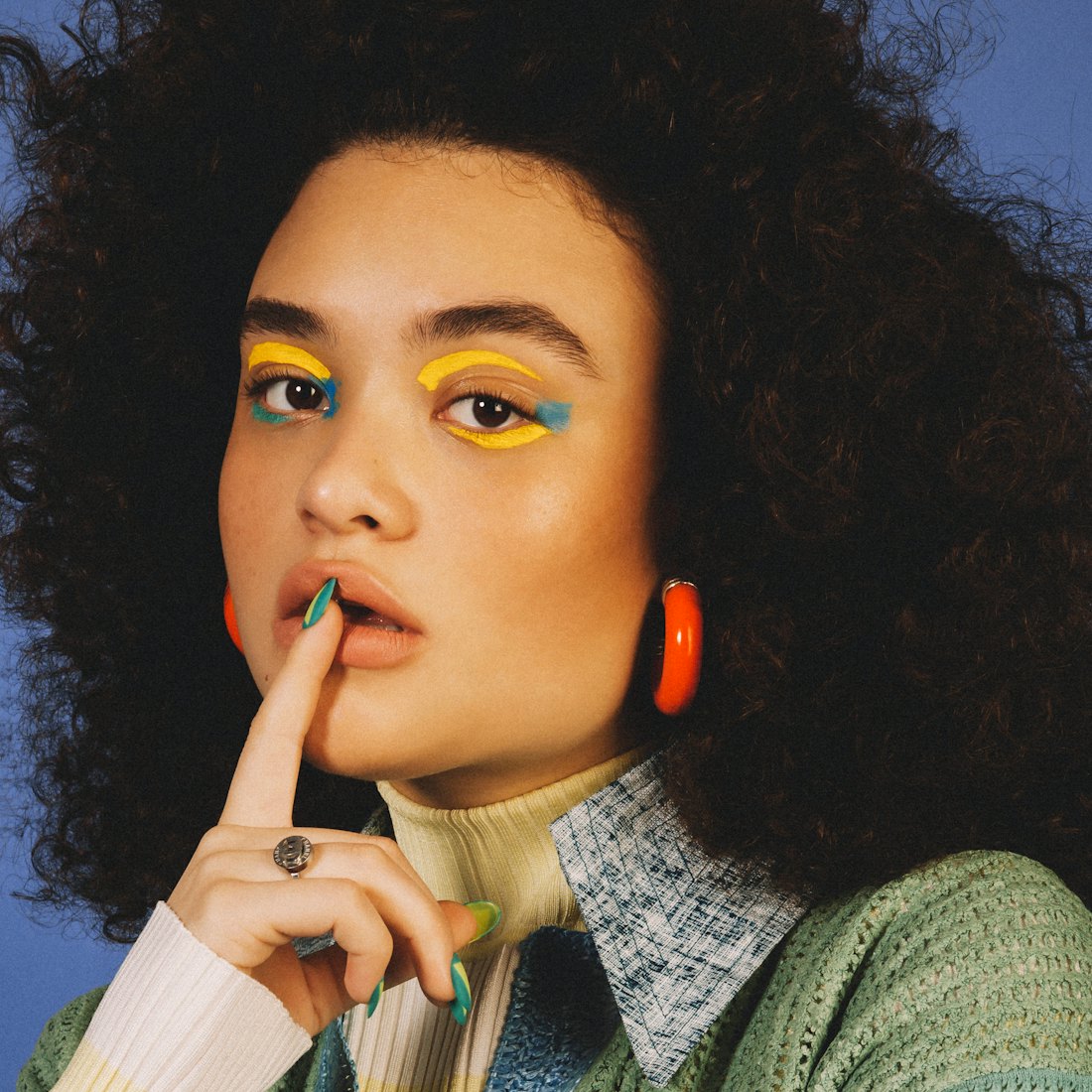 Diana Veras with yellow and blue eye make-up showing off her long nails and orange hoop earrings