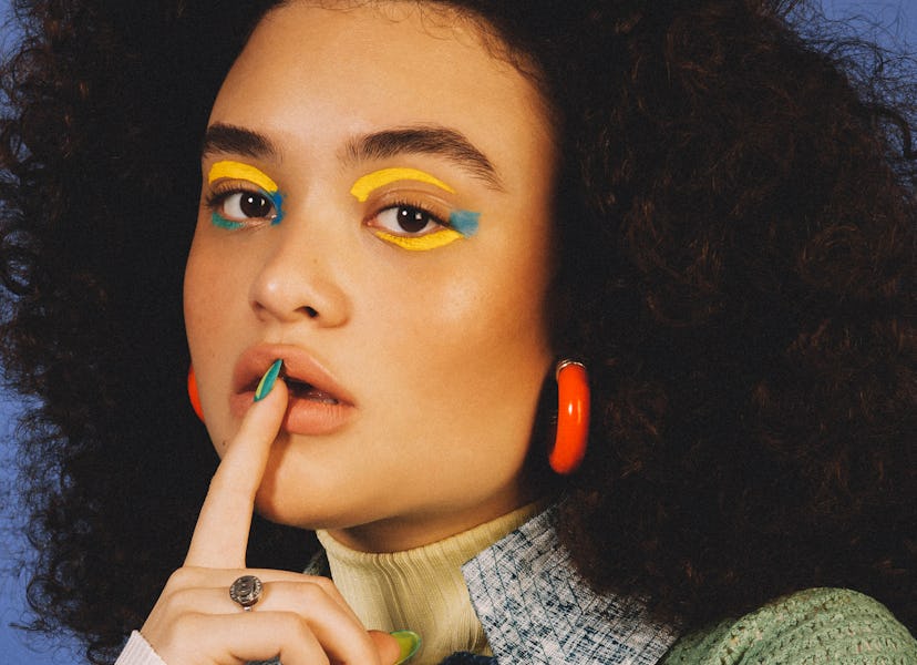 Diana Veras with yellow and blue eye make-up showing off her long nails and orange hoop earrings