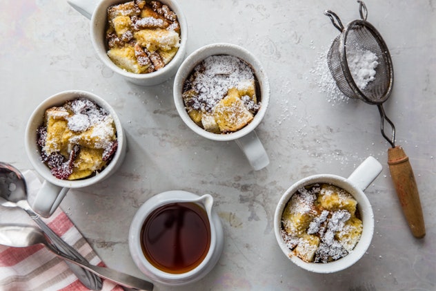 Image shot overhead of four mugs filled with french toast, one cup with syrup, and a powdered sugar ...