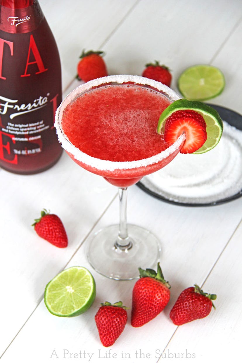 Margarita glass filled with strawberry wine slushie with fresh strawberries scattered at the bottom ...