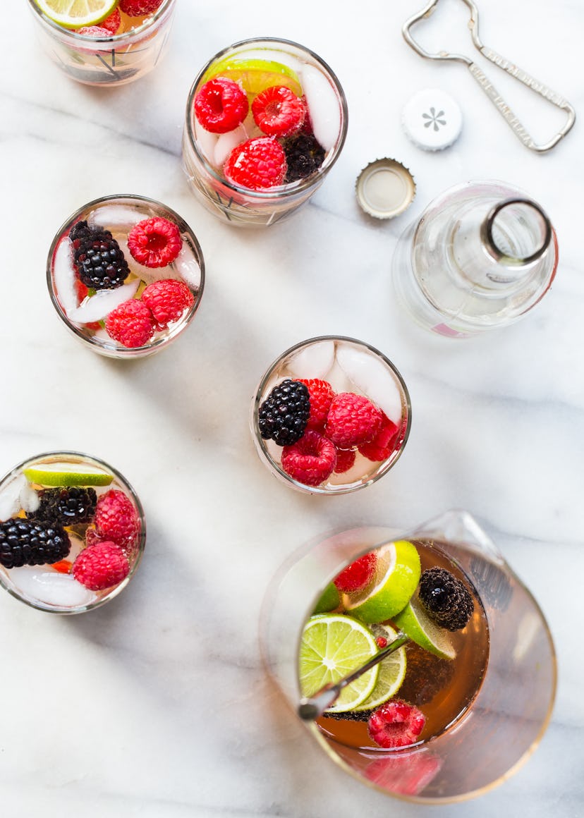 The top of several glasses full of sangria and topped with fresh limes, raspberries, and blackberrie...
