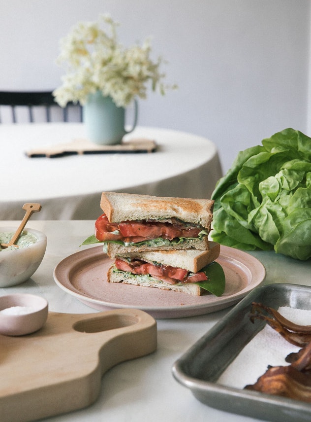 Counter top full of cookware and a white plate with halves of BLT stacked on top of each other