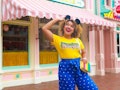 A happy woman with Mickey ears and a Disneyland shirt stands in the middle of Main Street at Disneyl...