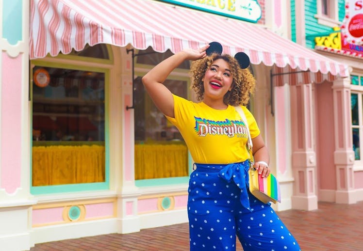 A happy woman with Mickey ears and a Disneyland shirt stands in the middle of Main Street at Disneyl...