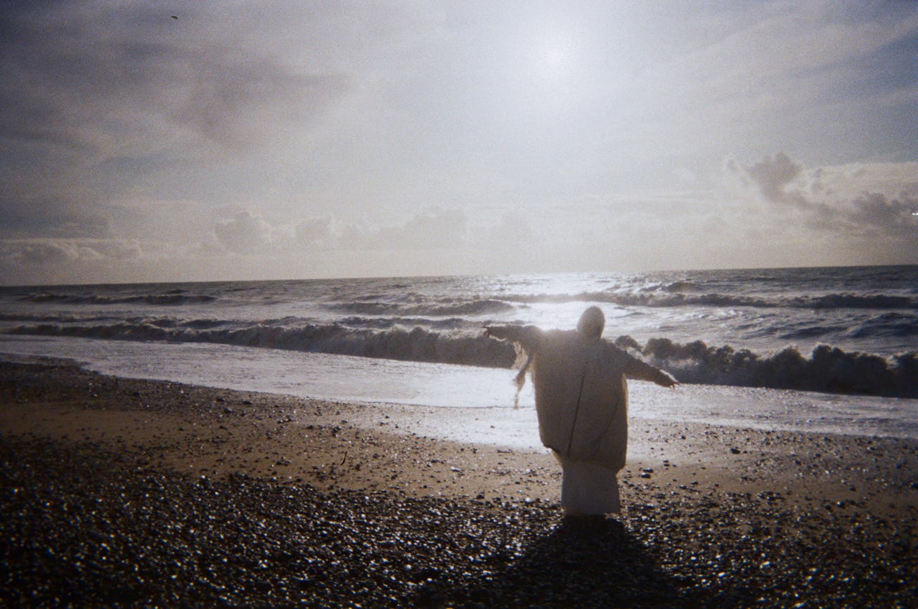 A bundled figure approaches the ocean.