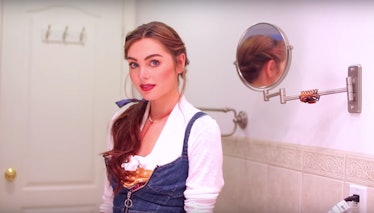 A woman in a jean outfit with a blue bow in her ponytail stands in her bathroom. 