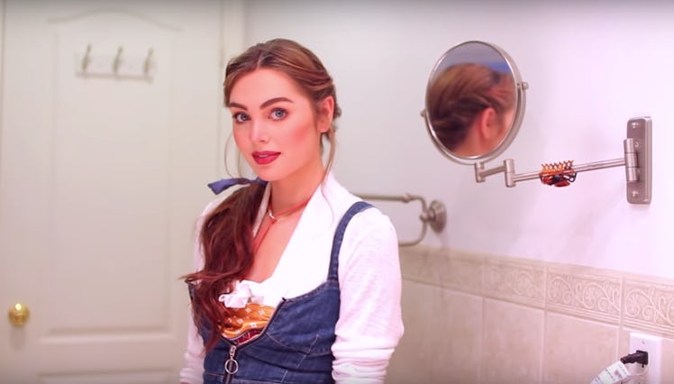 A woman in a jean outfit with a blue bow in her ponytail stands in her bathroom.