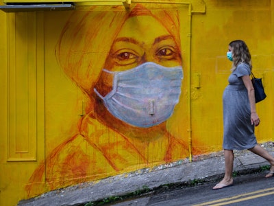 A pregnant woman walks past a street mural in Hong Kong on March 23, 2020. With the coronavirus pand...