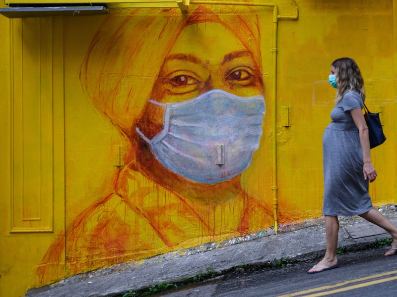 A pregnant woman walks past a street mural in Hong Kong on March 23, 2020. With the coronavirus pand...