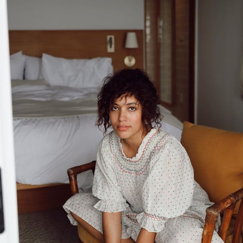 A woman in a white frilled puff-sleeved lingerie dress working from bed