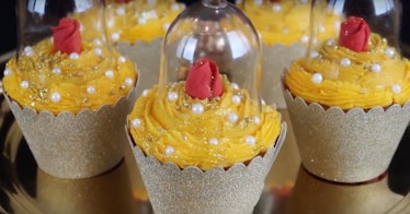 Five 'Beauty and the Beast'-themed cupcakes with red roses and yellow icing are placed on a cupcake ...