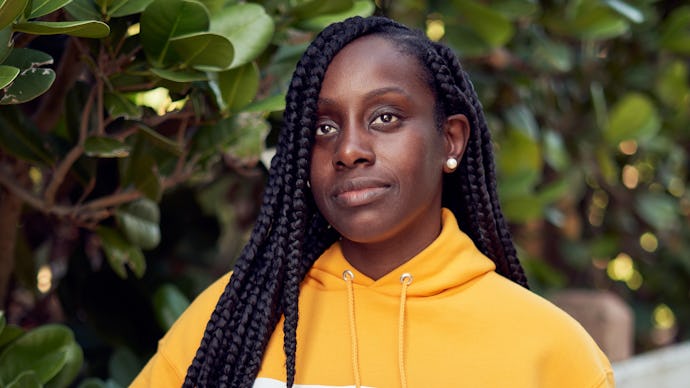 A woman with dreadlock hairstyle posing for a photo in a yellow hoodie
