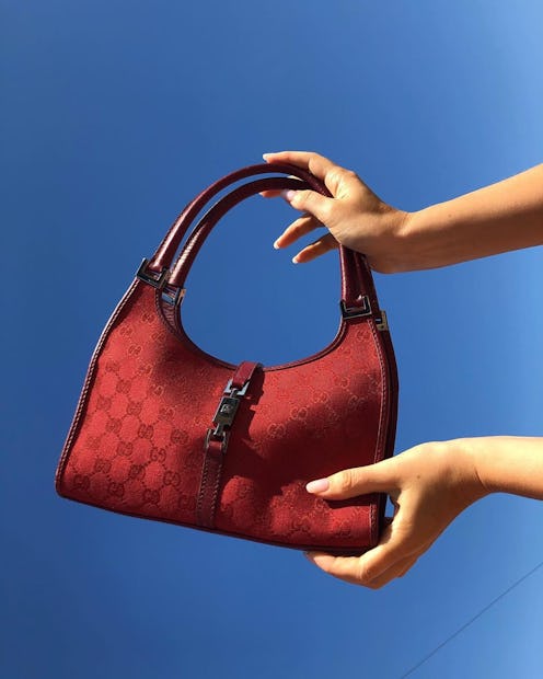 Hands holding a red vintage Gucci bag in front of a blue background