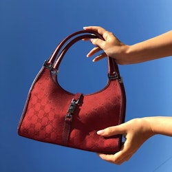 Hands holding a red vintage Gucci bag in front of a blue background