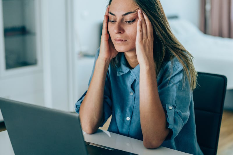 A person frowns as she rubs her temples, staring at her computer. Stress can impact your sleep, whic...