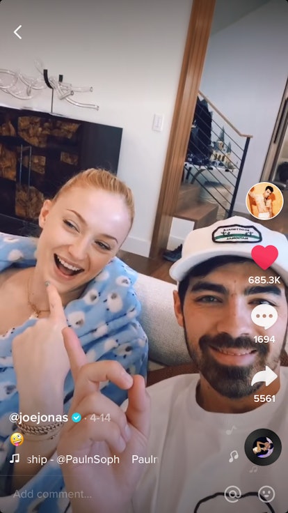 Joe Jonas and Sophie Turner point to each other, while sitting on their couch at home. 