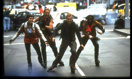 A group of four men rollerblading down a street
