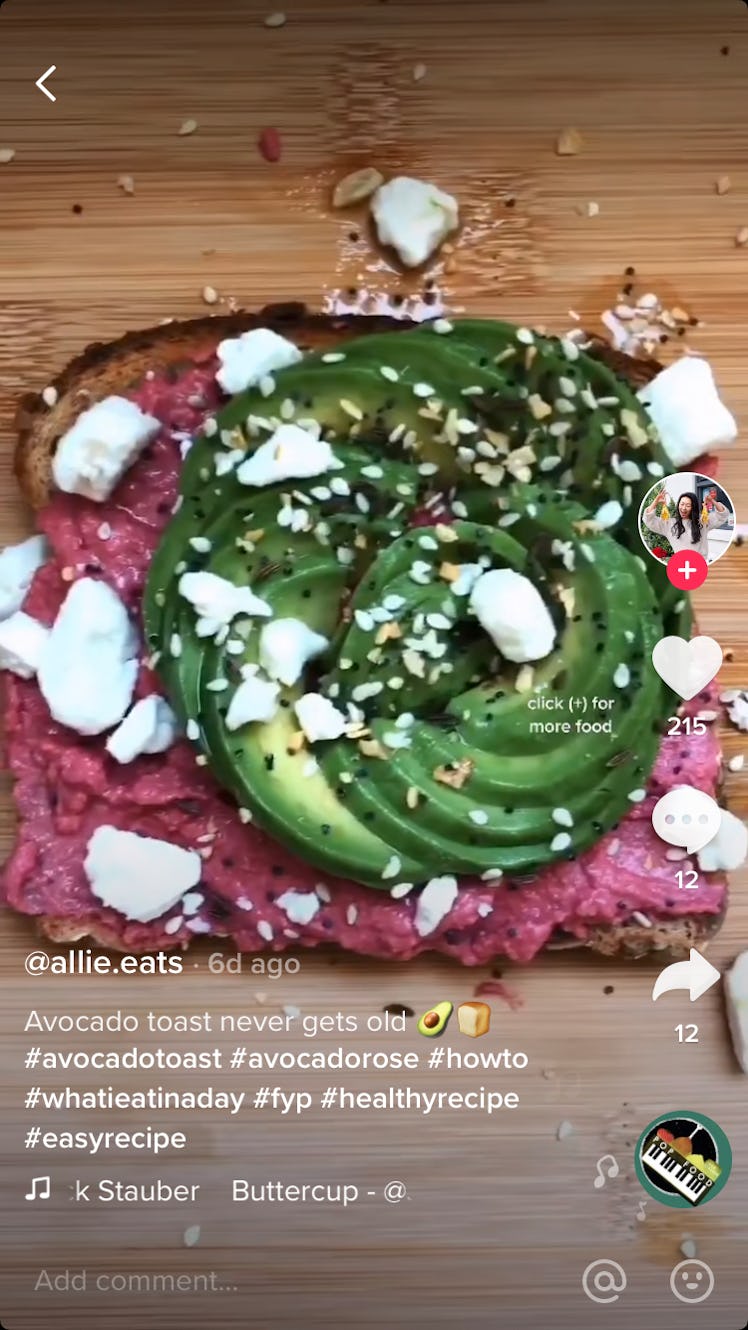 An avocado, shaped like a rose, sits on top of red beet hummus, with feta and bagel seeds sprinkled ...
