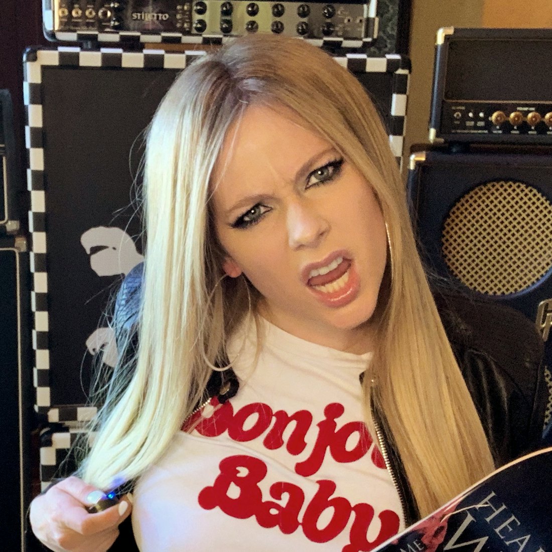 Avril Lavigne holding a skateboard surrounded by massive speakers.