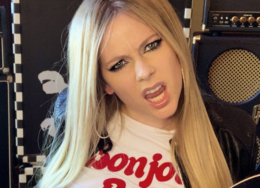 Avril Lavigne holding a skateboard surrounded by massive speakers.