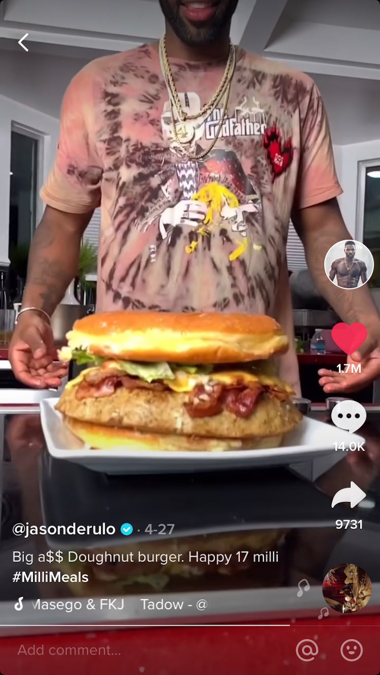 Jason Derulo goes to grab a giant donut burger that is sitting on a plate. 