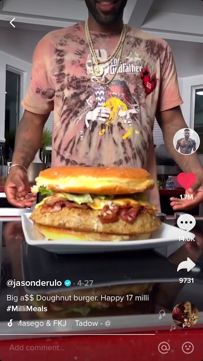 Jason Derulo goes to grab a giant donut burger that is sitting on a plate. 