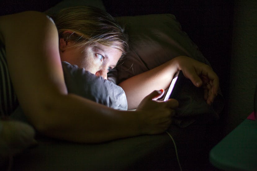 Woman lies in bed in the dark looking at phone