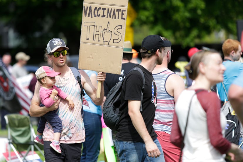 A man carries a child and an anti-vaccination sign as people protest outside the State Capitol in Ol...