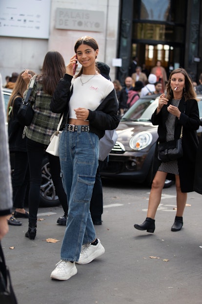 A girl wears wide cargo denim pants with a white crop top, a short, black bomber jacket, and a pair ...