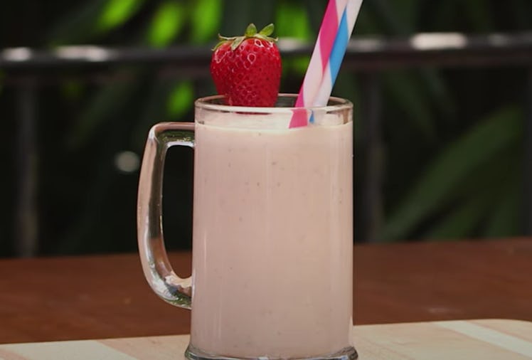 A mug filled with a peanut butter and jelly milkshake sits on a table with a strawberry decoration o...