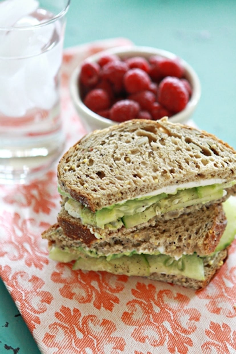 Cucumber Avocado Sandwich on a patterned dish cloth with a bowl of berries and a glass of ice water ...