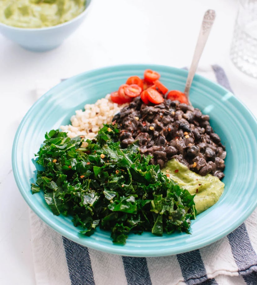 Blue bowl of kale, quinoa, black beans, avocado, and tomatoes sitting on a striped dish towel 
