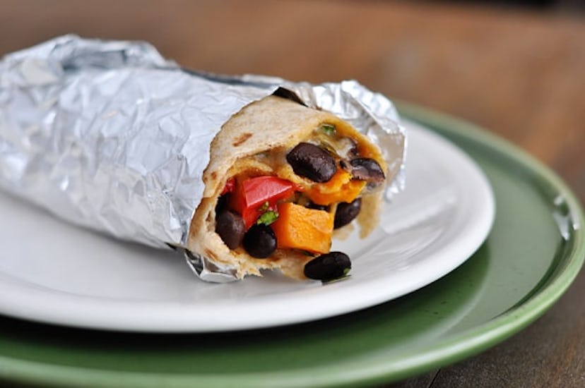 Black bean and sweet potato burrito (bottom half wrapped in foil) on white and green plates