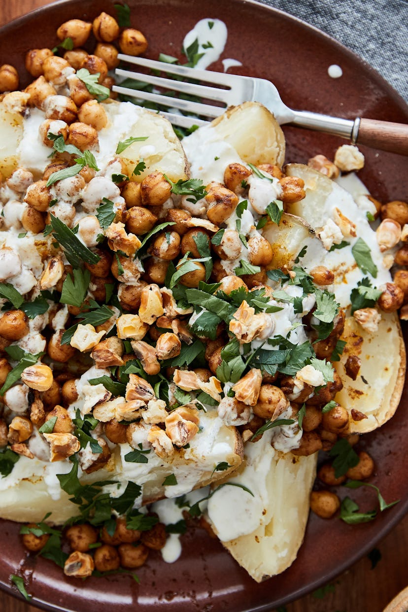 Plate of loaded potatoes with spiced chickpeas and a white drizzle on a burgundy plate